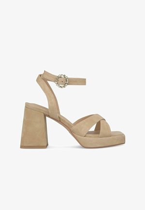 Beige Wildledersandale mit Blockabsatz, gekreuzten Riemen und Knöchelriemen mit einer runden Schnalle. Strukturierte Oberfläche und breiter Absatz.