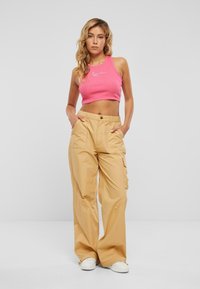 Rosa kortärmad topp med ribbad struktur, parat med beige cargobyxor som har knappstängning och sidofickor. Vita sneakers nedanför.
