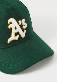 Grønn filtkaps med brodert hvit og gul "A's"-logo. Bøyd skjerm med synlige sømmer.