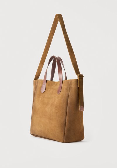 Borsa tote in camoscio marrone con doppi manici corti in pelle e tracolla lunga regolabile in camoscio su sfondo bianco.