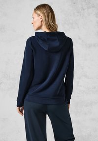 Marineblå hoodie med en glat tekstur, der har en snørehætte, lange ærmer og en løs pasform, parret med mørke bukser.
