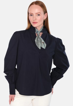 Marinblus med hög krage, rynkade detaljer och långa ärmar. Inkluderar en ljusgrön mönstrad scarf knuten vid halsen.