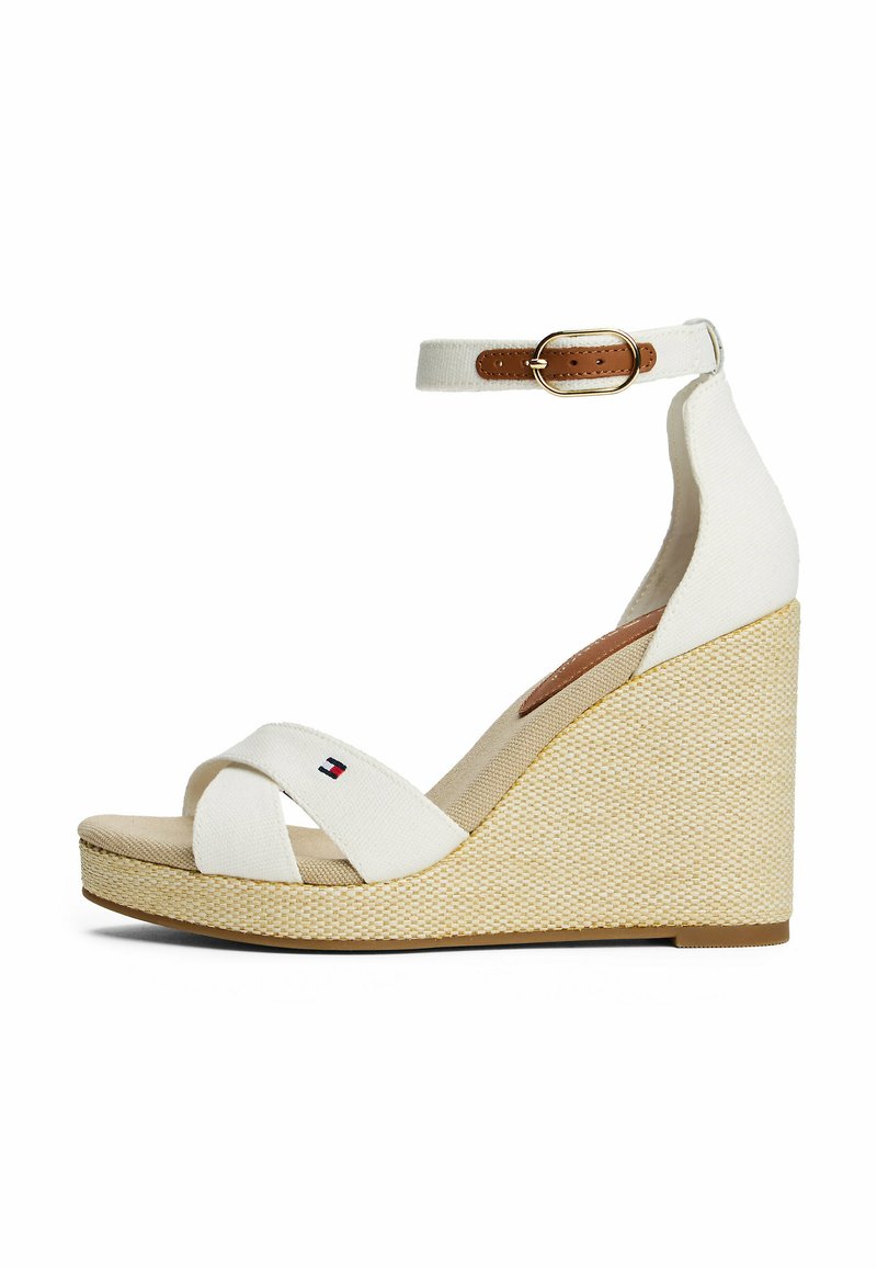 Sandalias de cuña blancas con suela de yute texturizado, diseño de tiras cruzadas y correa para el tobillo con un hebilla de cuero marrón. Detalle pequeño del logotipo visible.