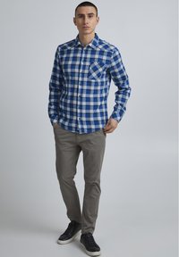 Blå og hvit rutete flanellskjorte med brystlomme, knappedesign, lange ermer og krage, kombinert med grå bukser og svarte sneakers.