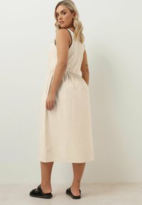 Kalkkimekko ilman hihoja, jossa on istuva yläosa ja levenevä hame, varustettuna kerättyllä vyötäröllä ja mustilla koristeilla. Yhdistetty mustiin liukuviin sandaaleihin.