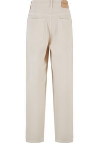 Pantalon beige à jambes droites avec poches arrière et passants de ceinture, avec une étiquette en cuir marron clair sur la ceinture.