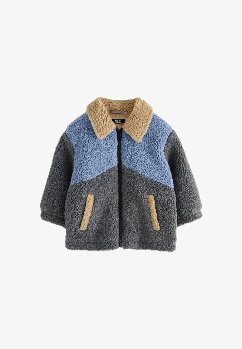 Veste en fausse fourrure avec fermeture éclair. Texturée en bleu, gris et beige. Dispose d'un col et de deux petites poches avant.