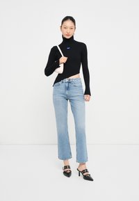 Maglione nero a costine con collo alto e orlo asimmetrico, abbinato a jeans azzurri a gamba dritta e tacchi neri con accenti argentati.