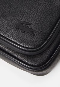 Borsa in pelle nera con finitura testurizzata, caratterizzata da un logo di coccodrillo nero in rilievo e bordi arrotondati accentuati da un trim elegante.