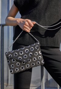 Clutch bag nera e argento con motivo esagonale e accenti metallici, dotata di una tracolla a catena per il trasporto. Finitura in tessuto testurizzato.