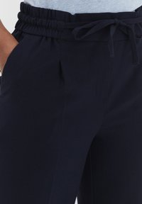 Navy blue elastic waist trousers with a drawstring, featuring side pockets and a smooth, soft texture.