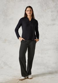 Polo shirt nero a maniche lunghe con colletto, abbinato a pantaloni grigi scuri a vestibilità ampia e sneakers bianche con dettagli marroni.