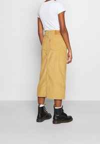 Kord midi kjol i ljusgul med en åtsittande midja, bakfickor och en logotyp patch. Matchas med svarta snörkängor.