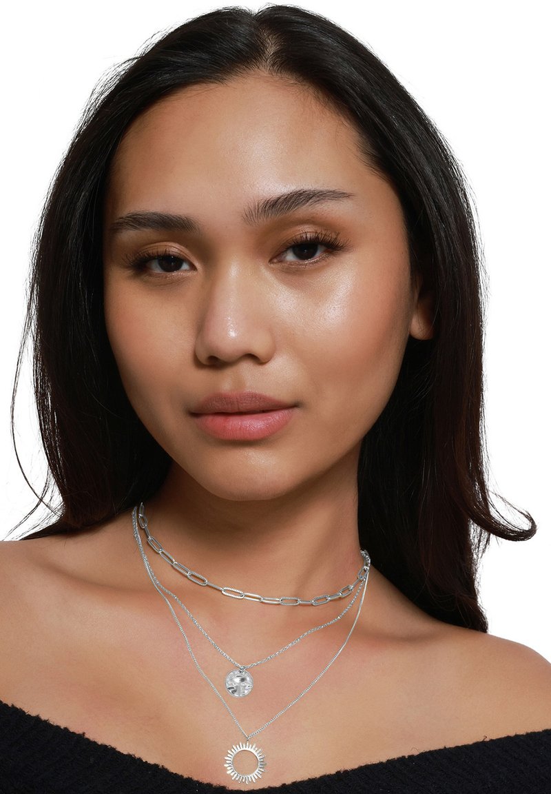 Zilveren halsketting set met een stevige schakelketting, een hangende ronde hanger en een zonnestraal charme, allemaal gelaagd tegen een donkere top.