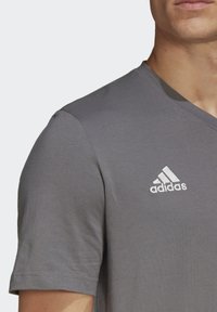 Gray cotton t-shirt with a v-neck design. Features embroidered white Adidas logo on the left side of the chest. Short sleeves.