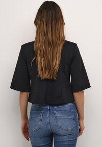 Svart avkortad topp med ärmar som når till armbågen, med en slät yta och skräddarsydd passform, tillsammans med blå åtsittande jeans.