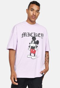 Světle fialové tričko s potiskem Mickey Mouse v červených šortkách. Volný střih, krátké rukávy, s malou černou nášivkou na lemu.