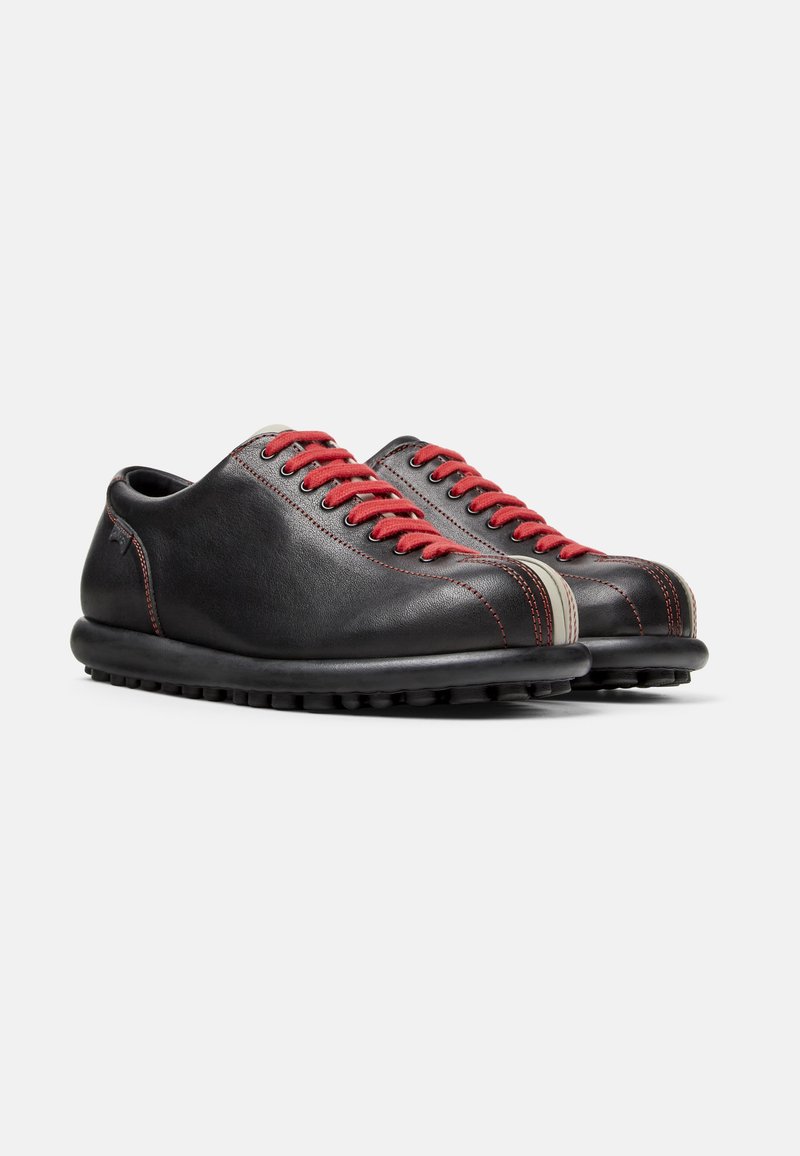 Zapatos de cuero negro con cordones rojos y rayas grises. Presentan una punta redondeada, suela negra texturizada y un diseño minimalista.