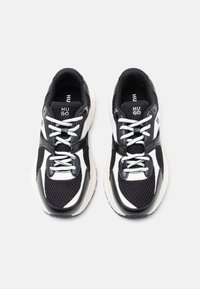 Chaussures de sport en noir et blanc avec une tige en mesh, une semelle en caoutchouc et des accents contrastants. Les lacets et le logo sont bien visibles sur la languette.