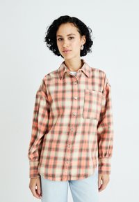 Flannel skjorte i orange, fersken og grøn ternet mønster. Har knaplukning foran, krave og en brystlomme. Blød tekstur.