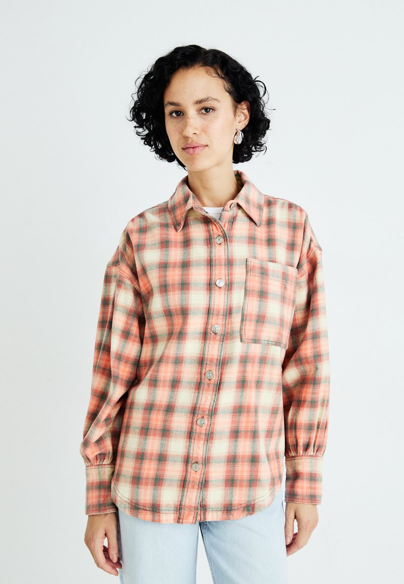 Flannel skjorte i orange, fersken og grøn ternet mønster. Har knaplukning foran, krave og en brystlomme. Blød tekstur.