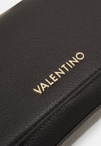 Czarna torba skórzana o teksturowanej powierzchni z złotym logo "VALENTINO". Design jest elegancki, z gładkim wykończeniem i uporządkowanym kształtem.
