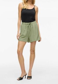 Zelené texturované šortky s elastickým pasem a stahovací šňůrkou, kombinované s černým tílkem a černými sandály s otevřenou špičkou.