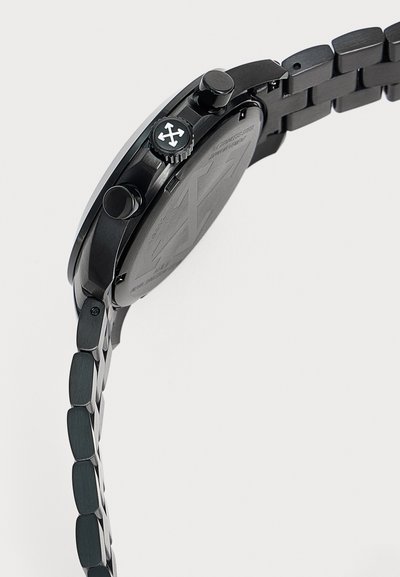 Montre-bracelet en métal noir avec un bracelet à maillons, des boutons latéraux et une couronne avec un symbole blanc à quatre flèches sur le côté du boîtier de la montre.