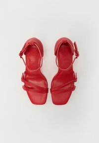 Sandales à talons en cuir rouge avec un bout carré, dotées de bretelles ajustables et d'une finition lisse, mettant en avant des détails de design minimaliste.