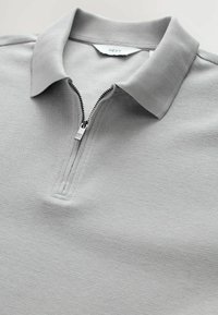 Lys grå tekstureret polo t-shirt med en delvist lynlås i metal og klippet krave, mærketag med teksten "NEXT" indeni halsudskæringen.