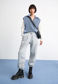 Gestreifter blauer und weißer Strickpullover, graue Sweatpants, schwarze Schnürplattformstiefel und eine schwarze Umhängetasche, alles vor einem hellen Hintergrund.