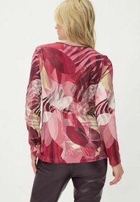 Top met lange mouwen met een gemengd bloemen- en abstract patroon in tinten rood, roze en beige, met een ronde halslijn en een zachte textuur.