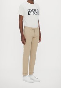 Beige chinos med slim fit, matchade med en vit t-shirt med en stor "POLO" grafik i marinblått. Bärs med vita sneakers.