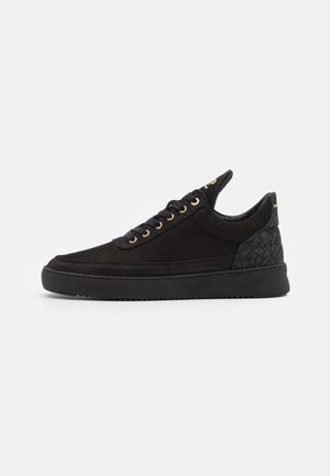 Black low-top sneaker with textured heel, gold eyelets, black laces, and thick sole on white background.