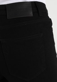 Vaqueros de mezclilla negra con un parche de cuero de la marca, costuras en los bolsillos traseros y un diseño ajustado con una textura suave.