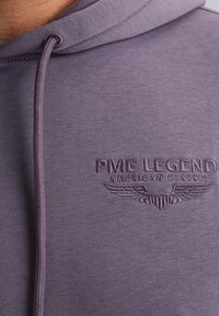 Paarse hoodie met een gestructureerde stof, verstelbare capuchon en geborduurd logo met vleugelaccenten. Zachte en gladde textuur.