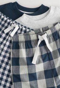 Trois paires de shorts présentent des ceintures élastiques, dont des motifs à carreaux bleu marine et gris, avec des cordons blancs et des étiquettes à l'intérieur.