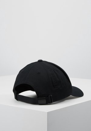Casquette de baseball noire réglable placée sur une surface blanche en angle, vue de dos avec une sangle et une boucle métallique.
