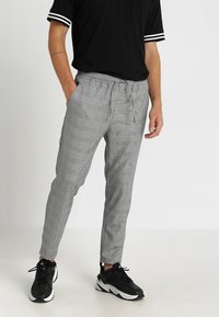 Šedé joggingové kalhoty s elastickým pasem, postranními kapsami a tapered střihem, zkombinované s černým tričkem a teniskami.