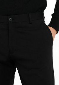 Schwarze Hose aus glattem Stoff, mit einem Knopfverschluss, Gürtelschlaufen und Seitentaschen, im Slim-Fit-Design.
