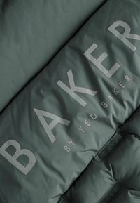 Grüner gesteppter Stoff mit großem, geprägtem "BAKER"-Text von Ted Baker, der eine glatte Textur und einen subtilen Glanz aufweist.