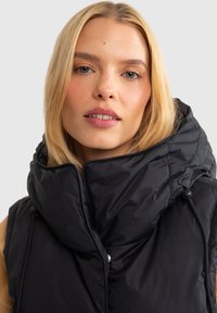 Musthave must vest must elav põhja ja oversized kapuutsiga, millel on sile tekstuur, õmbluse detailid ja külgfistikolvid.