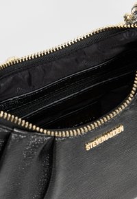 Sort håndtaskeinteriør med en lynlås, der har en glat tekstur, guldhardware og flere kompartments til organisering.