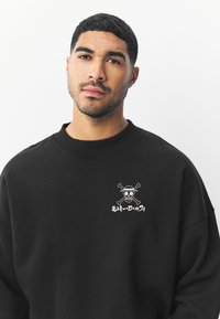 Sort sweatshirt lavet af bomuldsblanding med rund hals og løs pasform. Hvid kraniegrafik med korslagte knogler på brystet.