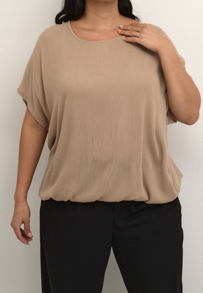 Beige, losvallend top met een ronde halslijn en korte mouwen, gemaakt van een lichte stof met een lichte glans, gecombineerd met zwarte broeken.