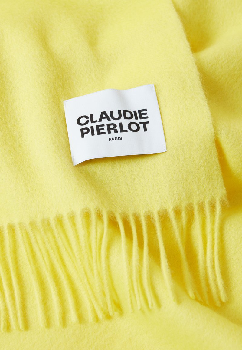 Gelber Wollschal mit fransigen Kanten. Besitzt ein Stoffetikett mit "CLAUDIE PIERLOT" und "PARIS" in Schwarz bedruckt. Weiche Textur.
