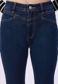 Jeans de mezclilla azul oscuro de talle alto, con costuras en contraste, cierre frontal de botón y un acabado suave y texturizado.