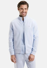 Veste zippée bleu clair en tissu doux, dotée d'un col haut et de poignets côtelés, associée à un t-shirt et un pantalon assortis bleu clair.