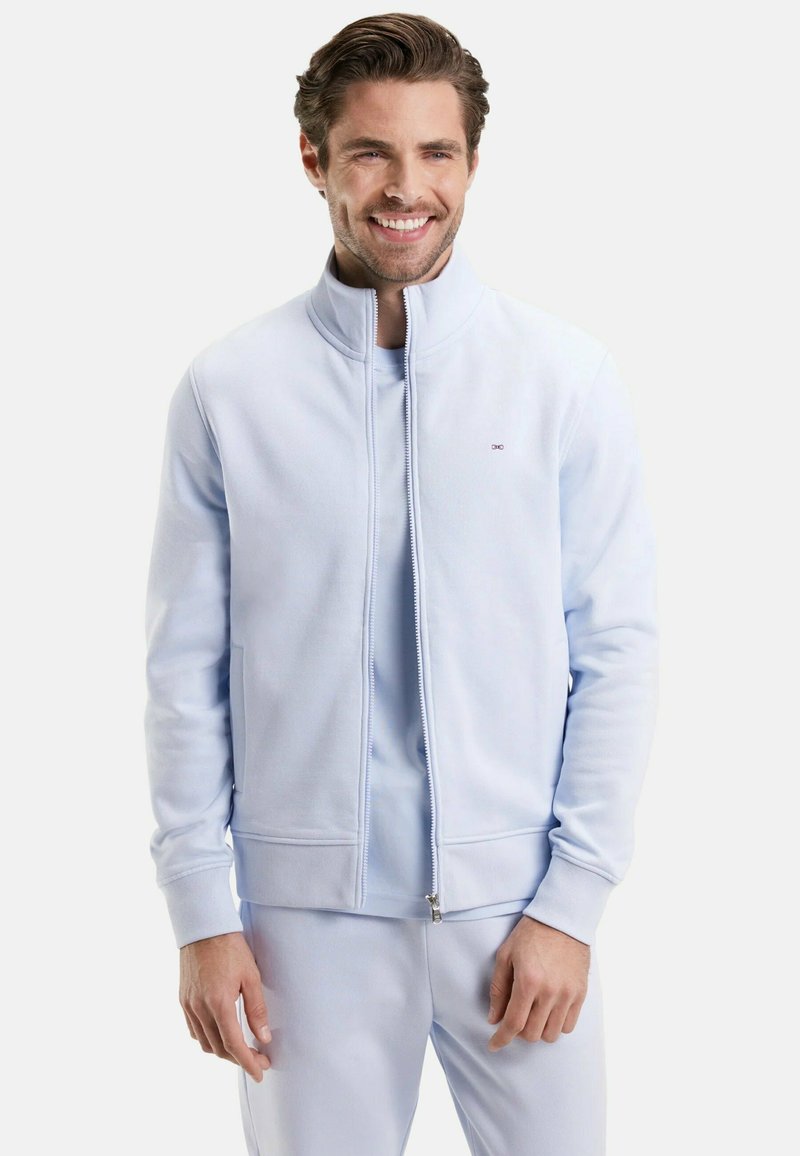 Veste zippée bleu clair en tissu doux, dotée d'un col haut et de poignets côtelés, associée à un t-shirt et un pantalon assortis bleu clair.
