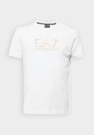 T-shirt in cotone bianco con logo beige EA7 e testo "EMPORIO ARMANI", collo rotondo e maniche corte, texture liscia.